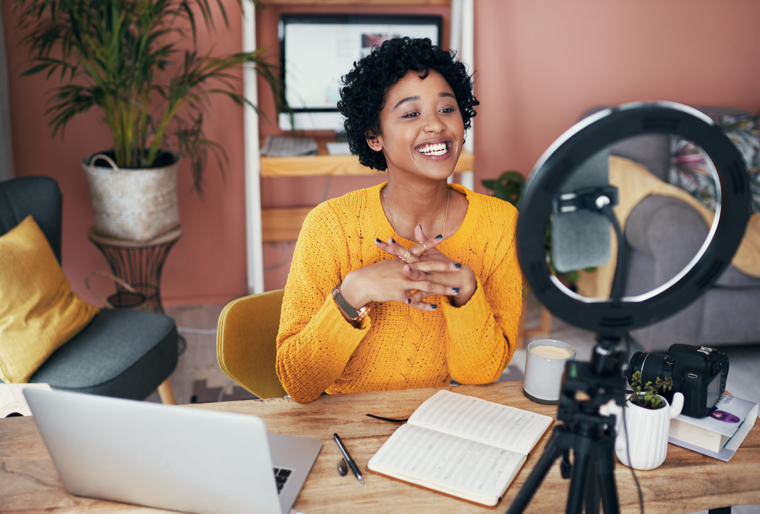 an influence live streams using a phone and ring light while smiling at her desk