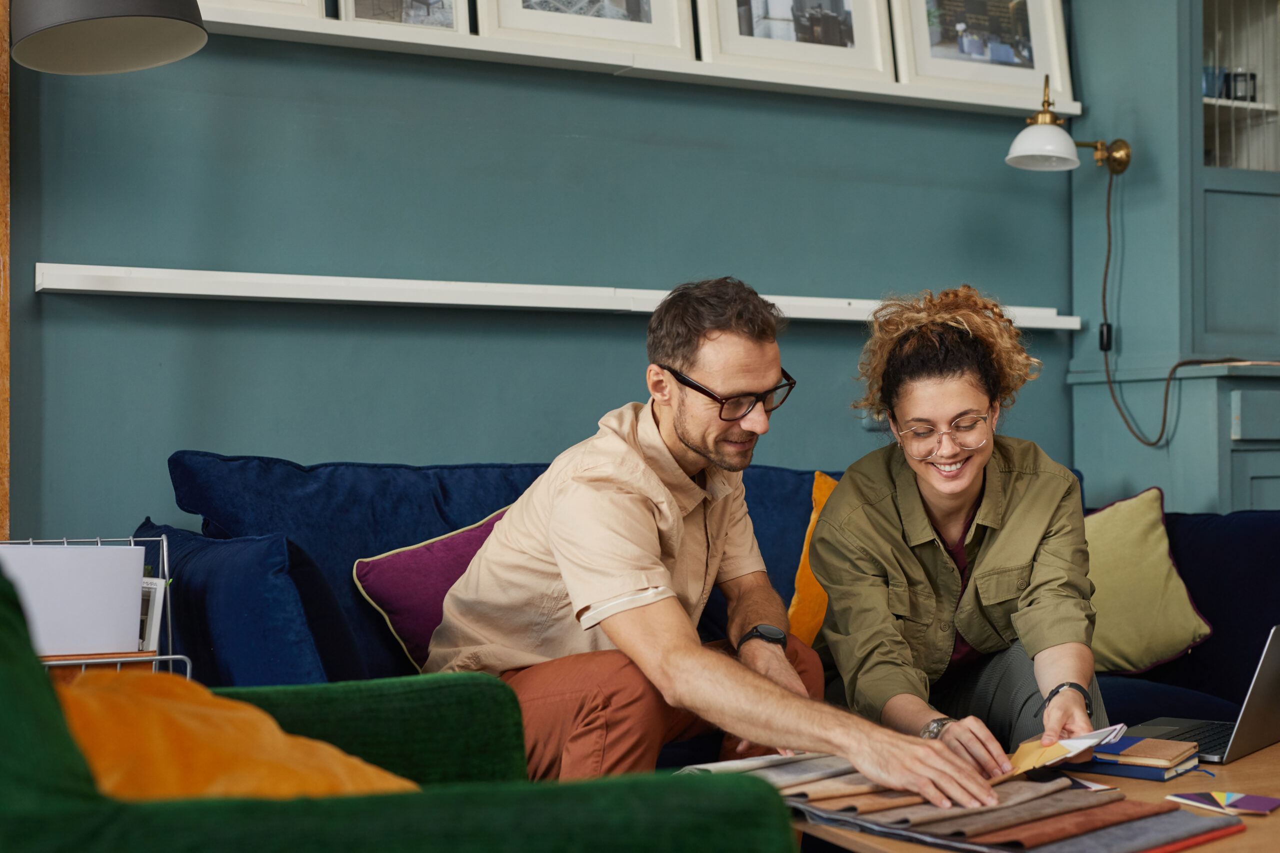 Two creators for a home and goods brand sitting on sofa and examining new collection of fashion fabric samples in a modern office