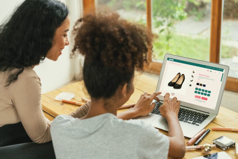 Two women shopping online at a laptop, looking at shoes on the screen
