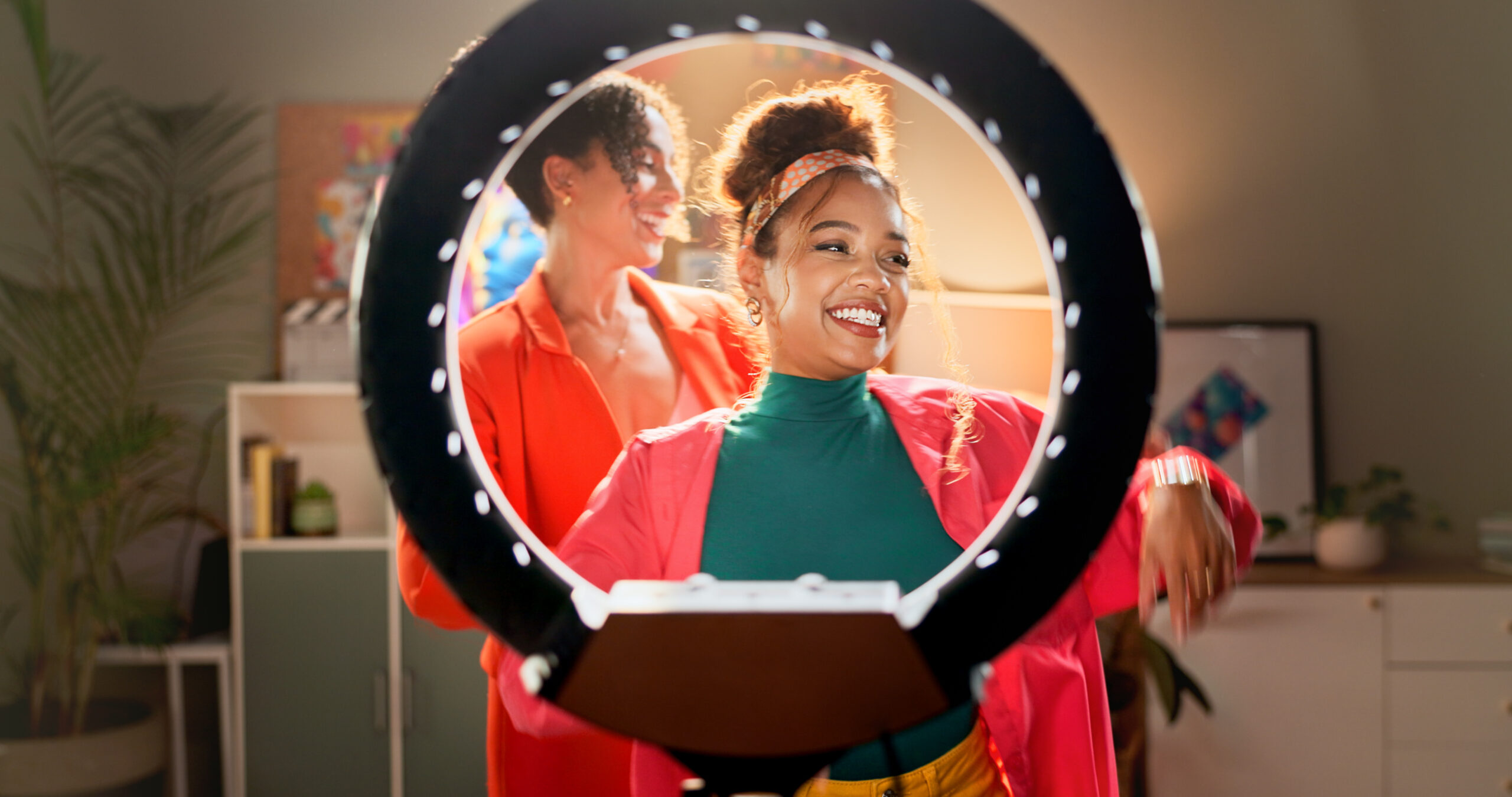 Two women influencers laugh and smile in front of a ring light camera