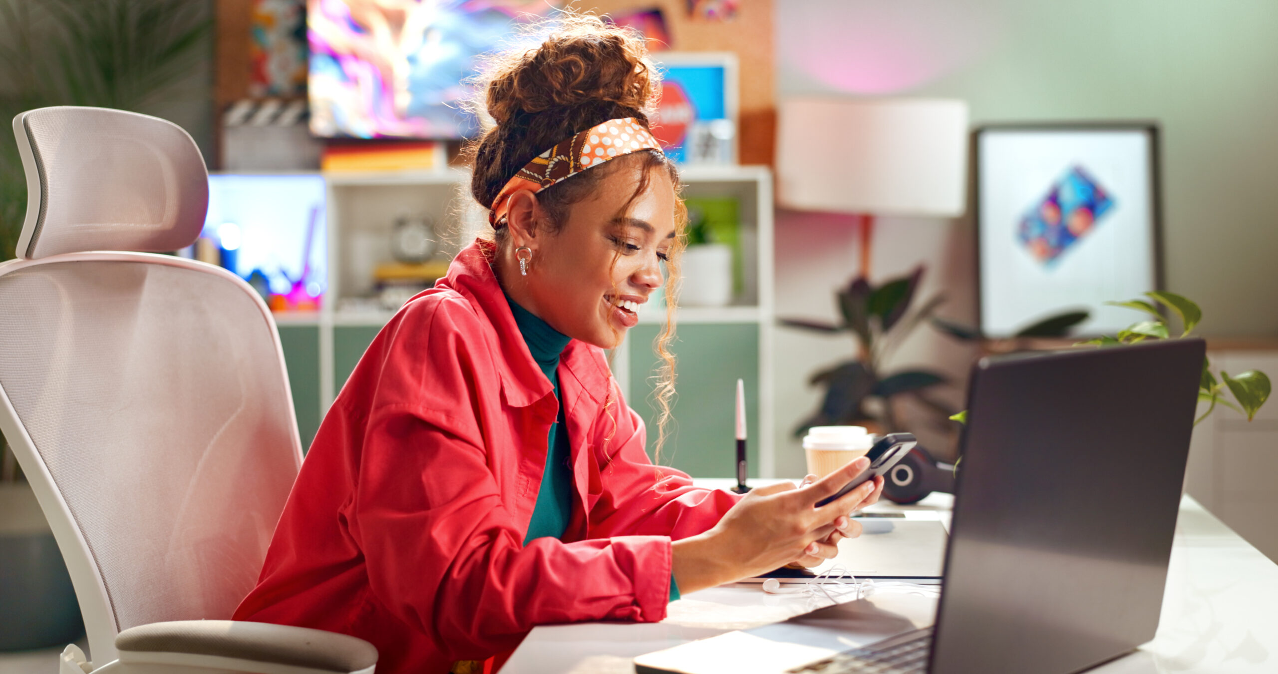A business woman smiles while looking at her phone with her laptop open